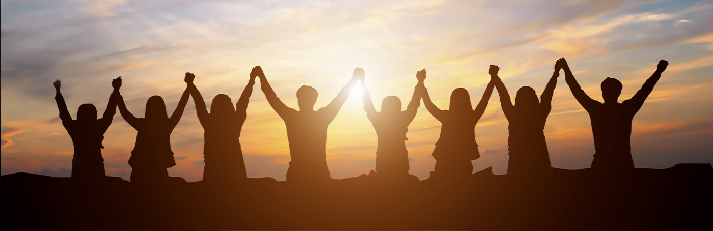 A silhouetted image of a line of people holding hands in the air facing a sunrise