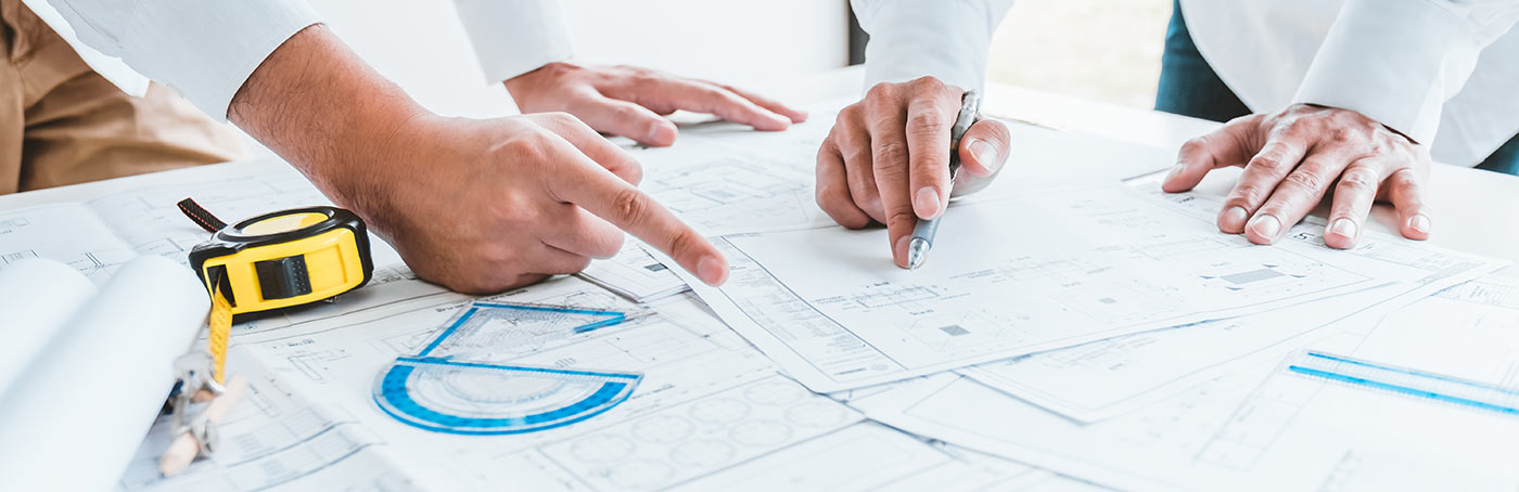 Image of people pointing to blueprints on a table with a tape measurer and tools on the table