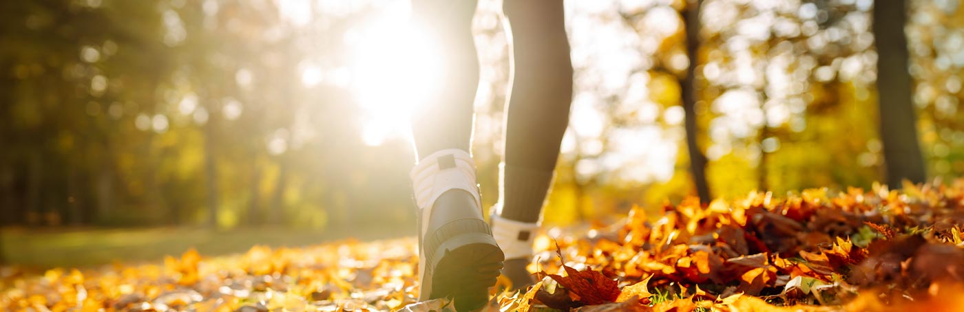 An image of a woman's feet, walking on a trail covered in Autumn leaves